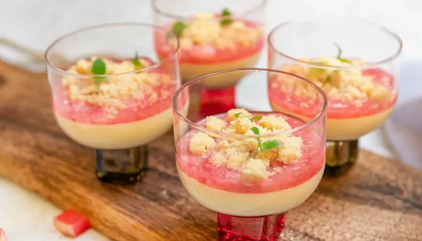 Fyra glas med krämig pannacotta med rabarberkompott och smuldeg. Garnerad med mynta. En härlig sommardessert.
