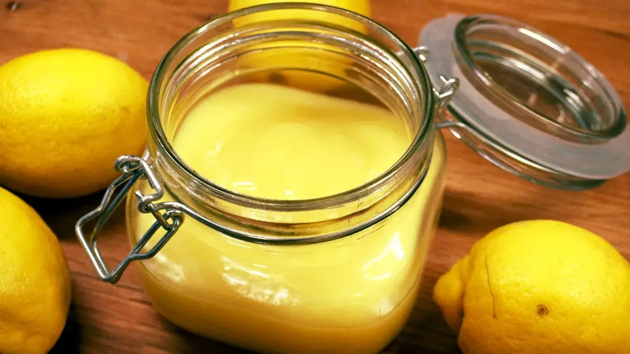 En burk med krämig, solgul lemon curd omgiven av färska citroner. Perfekt för bakning eller som tillbehör.