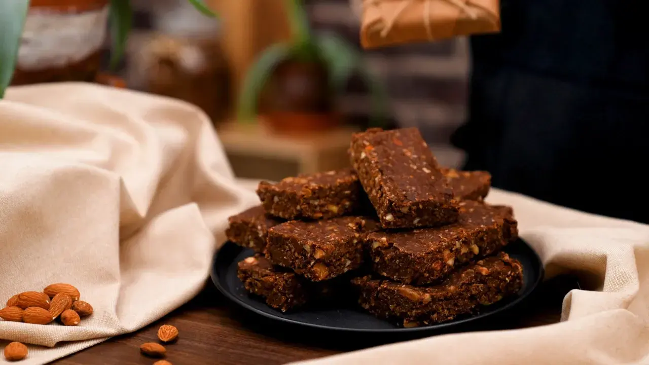 En hög med chokladdoppade dadlar och mandlar på en svart tallrik, omgivna av en ljus duk.