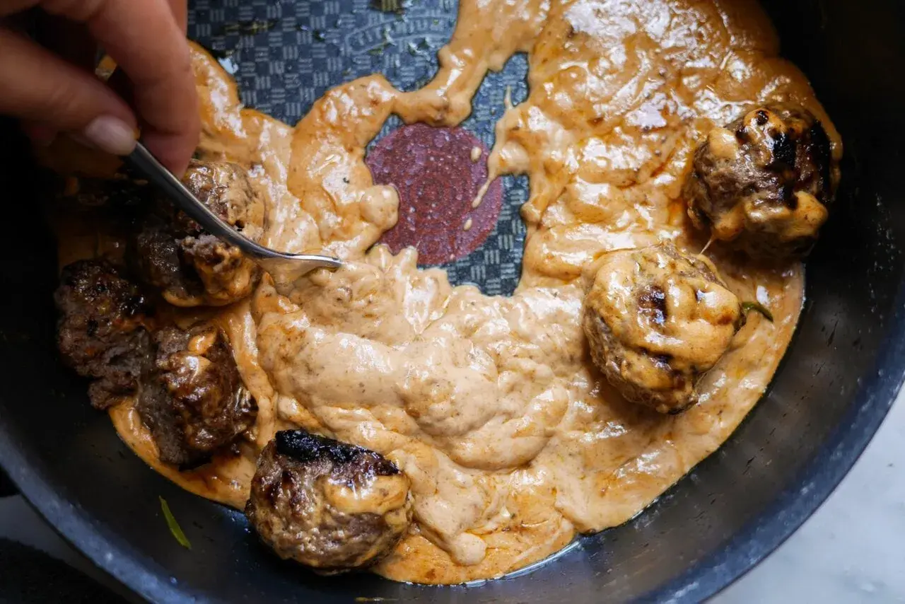 Köttbullar i krämig sås, perfekt tjocknad med maizena istället för potatismjöl. En gaffel rör om i den gyllene såsen.