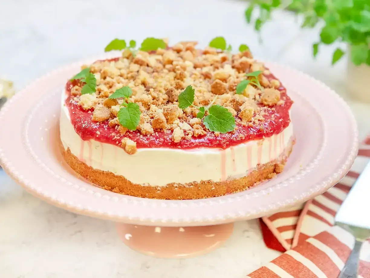 En läcker vit choklad cheesecake med hallon och smulor, dekorerad med mynta. Perfekt för fikat!