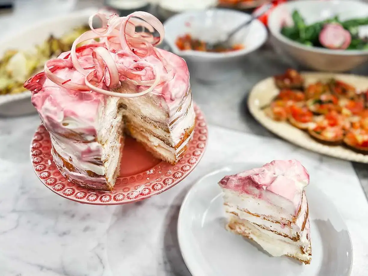 En vacker rabarberkompott tårta med rosa frosting och en skiva upplagd. Perfekt för en somrig fika.