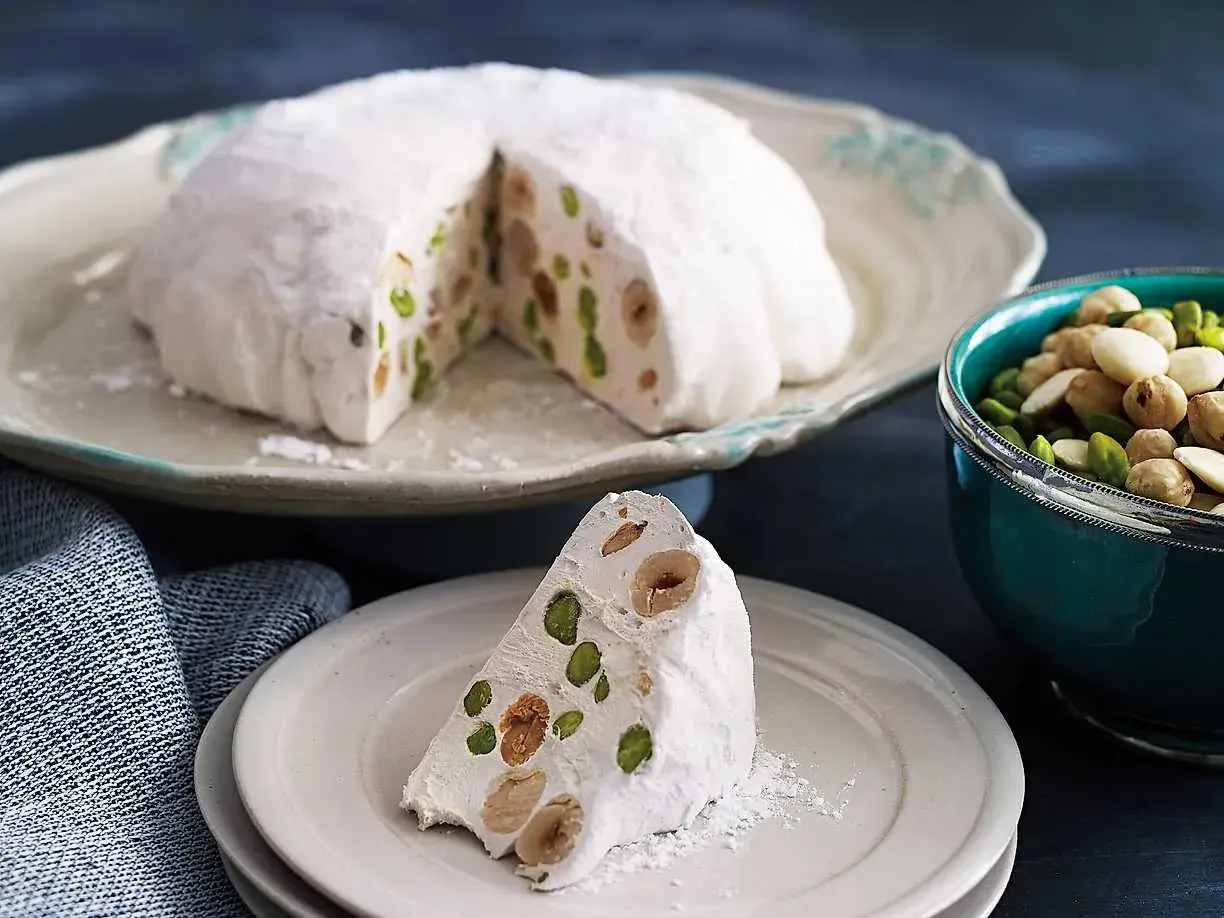 En bit av en vit nougatkaka med nötter och pistagenötter, perfekt att baka med nougat.