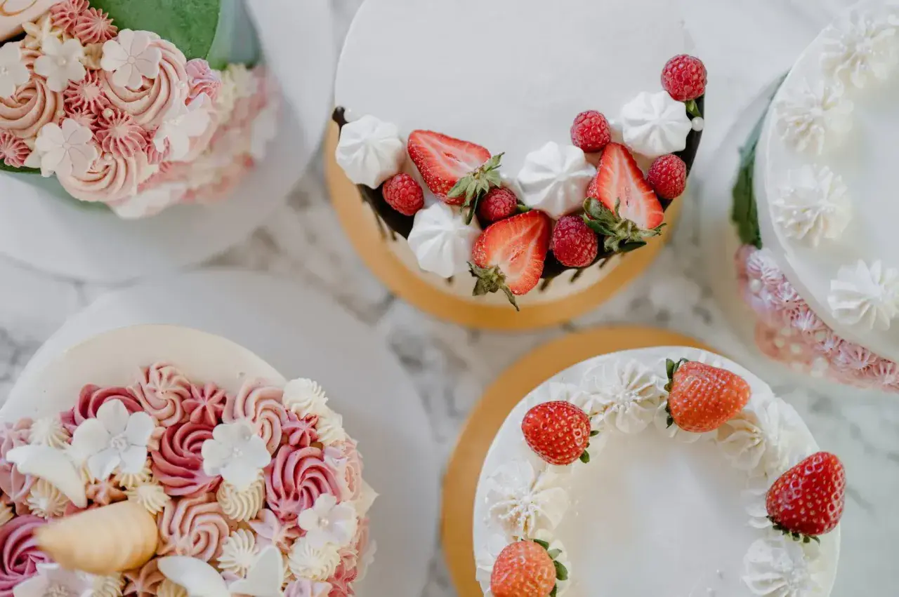 Flera vackra tårtor med fantasifulla dekorationer. En tårta är dekorerad med jordgubbar och maränger, en annan med rosa och vita blommor i frosting. Det är en festlig syn att dekorera tårta!