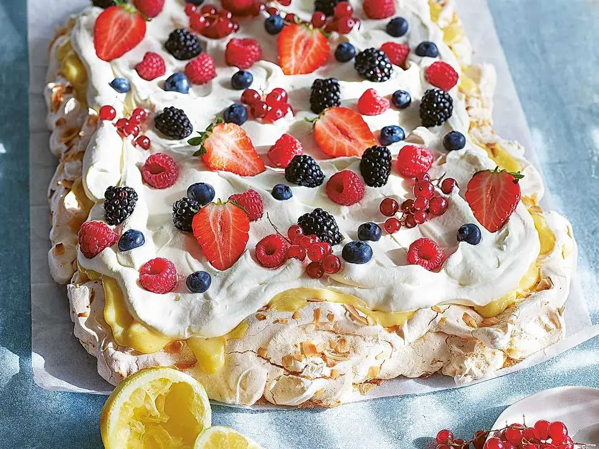 En stor pavlova i långpanna, täckt med vispgrädde, lemon curd och massor av färska bär som jordgubbar, hallon, blåbär och vinbär.