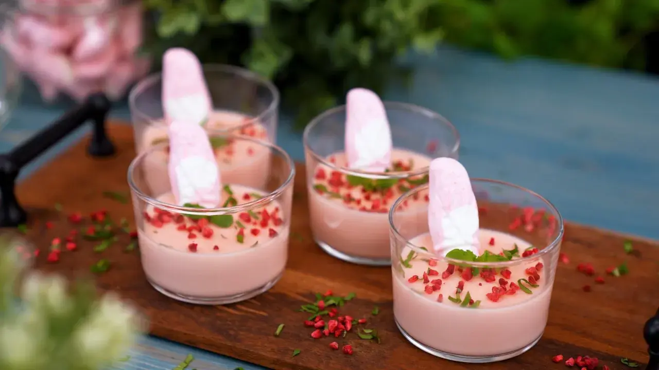 Fyra glas med rosa juleskum pannacotta, toppade med marshmallows, mynta och torkade hallon.
