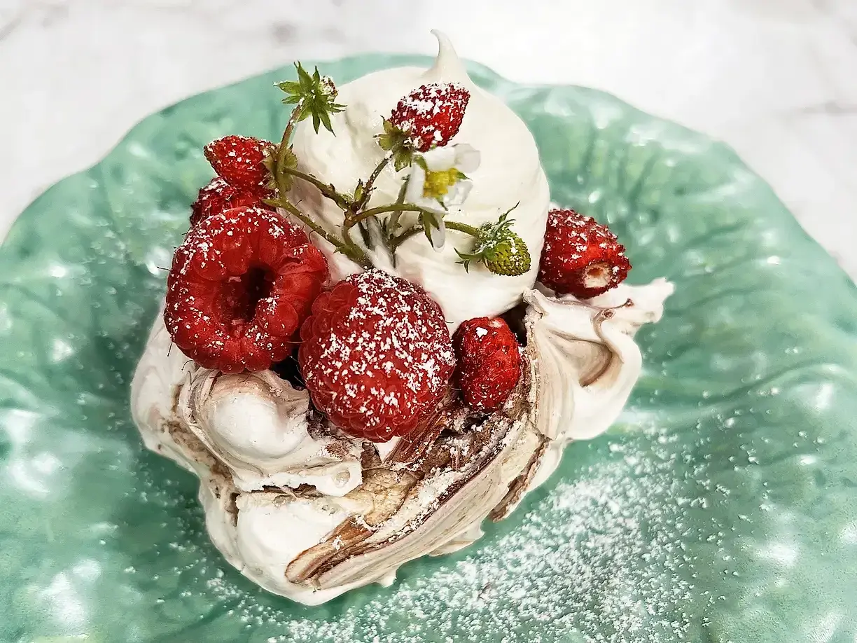 En härlig pavlova choklad med vispgrädde och färska bär, pudrad med florsocker på en grön tallrik.