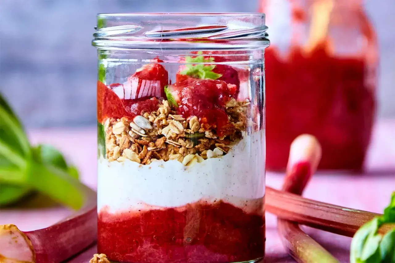 En glasburk med lager av rabarberkompott, yoghurt och granola. Rabarber är giftiga efter midsommar, men denna dessert är säker att njuta av.