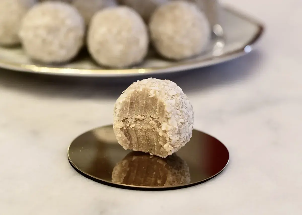 En närbild på en bit av en vit chokladboll, rullad i kokosflingor, med fler chokladbollar i bakgrunden.