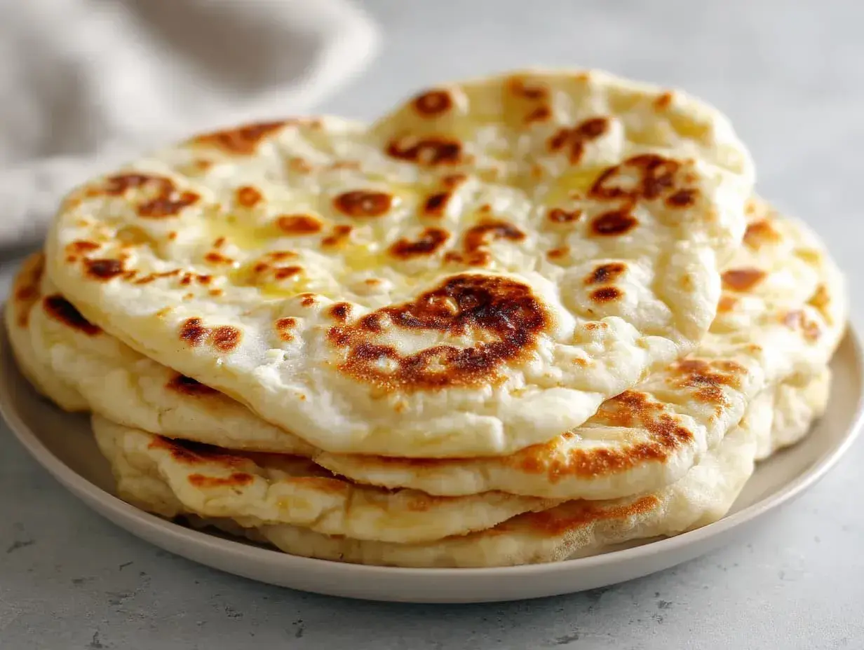 En hög med fluffigt, gyllene naanbröd, perfekt för ditt nästa naan recept. Smält smör glänser på toppen.