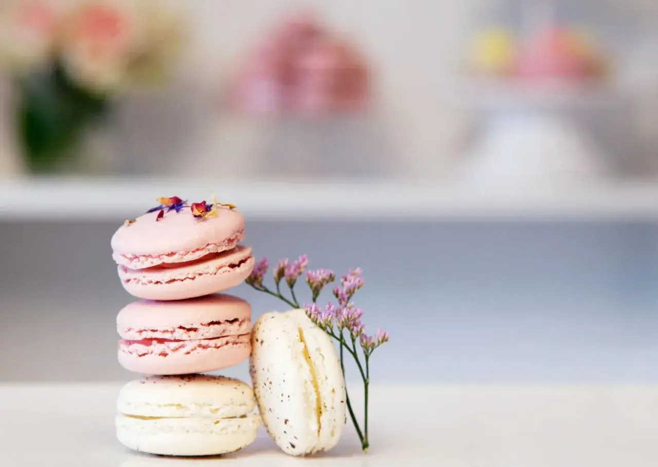 En stapel rosa och vita macarons, dekorerade med blomblad och en liten lila blomma. Perfekt för essenser bakning.