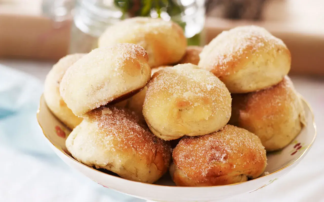 En skål med nybakade bullar, perfekt för att baka med söt jäst. De är pudrade med socker och ser aptitliga ut.