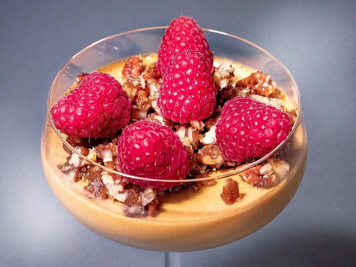En krämig dulce de leche pannacotta toppad med färska hallon och nötter i ett glas.