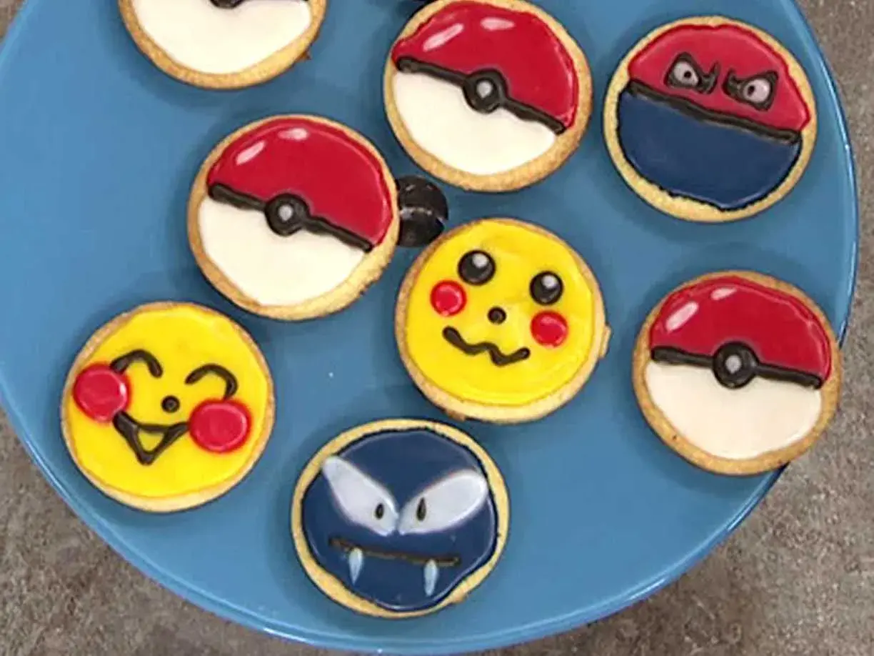 Sju dekorerade kakor på en blå tallrik, inklusive Pikachu, Pokémons och en Gastly. En härlig pokemon tårta för alla fans!