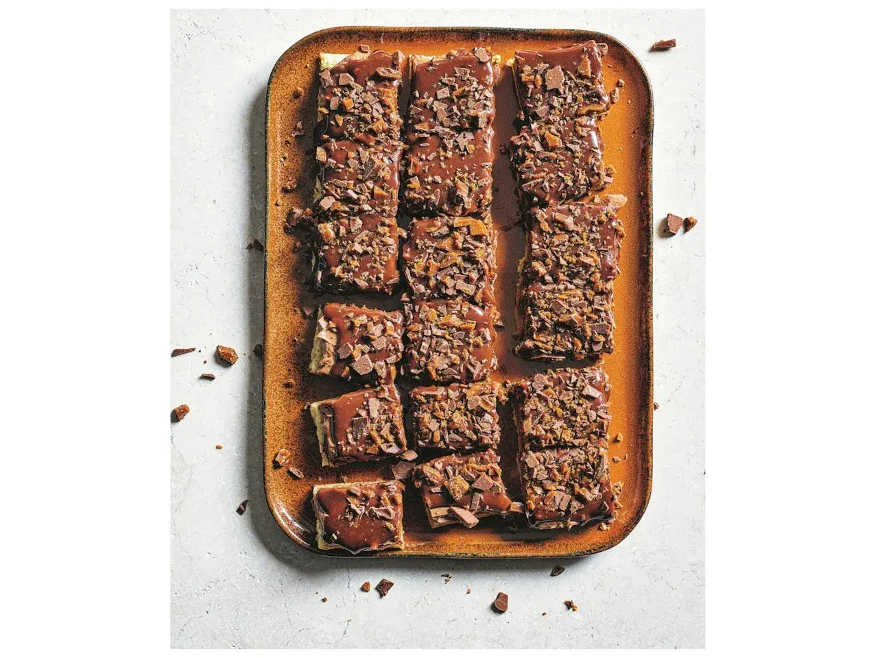 Chokladiga bitar av zserbó recept på en orange bricka, toppade med chokladglasyr och krossad choklad.