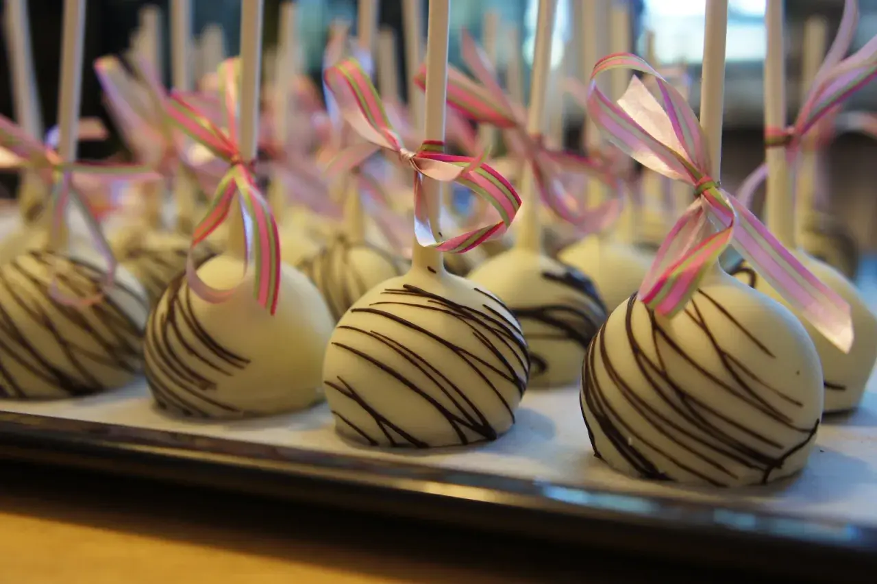 Vita cake pops med chokladmönster och rosa/gröna band. Perfekta för ett festligt tillfälle, som ett enkelt recept på oreo-bakverk.