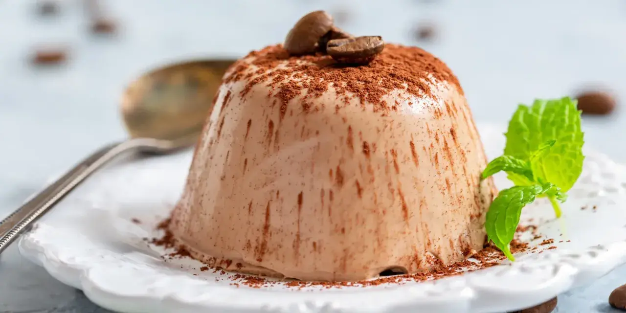 Krämig kaffepanna cotta toppad med kakaopulver och kaffebönor, garnerad med mynta.