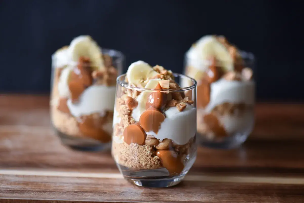 Tre glas med banoffee paj i lager av kexsmulor, krämig fyllning, banan och kolasås.