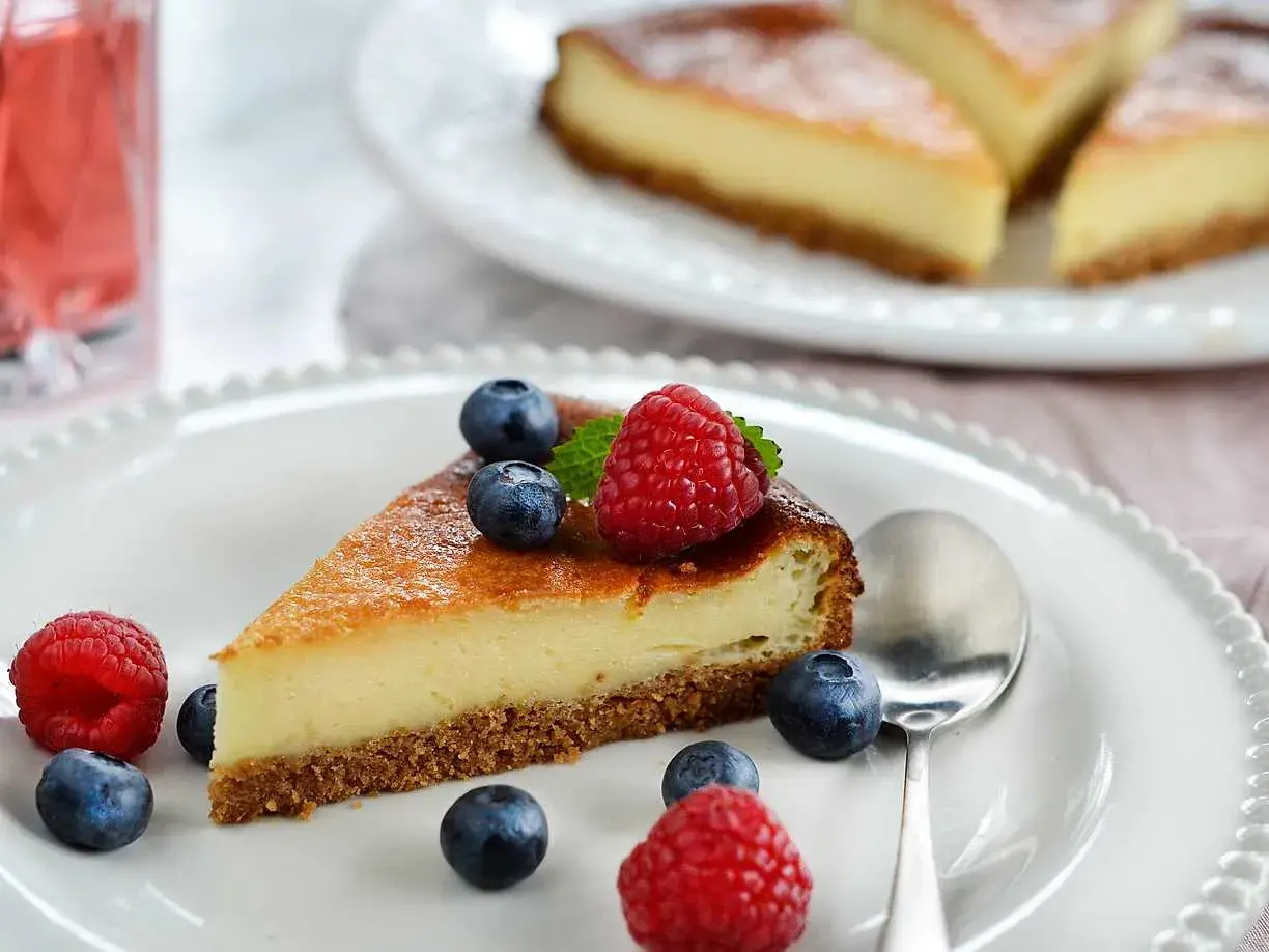 En bit krämig cheesecake med digestivebotten utan ugn, dekorerad med färska bär och mynta.