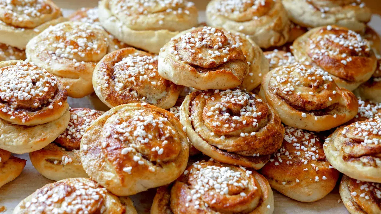 En hög med gyllene kanelbullar, toppade med pärlsocker. Perfekt för fikat, här är ett enkelt kanelbullar recept.
