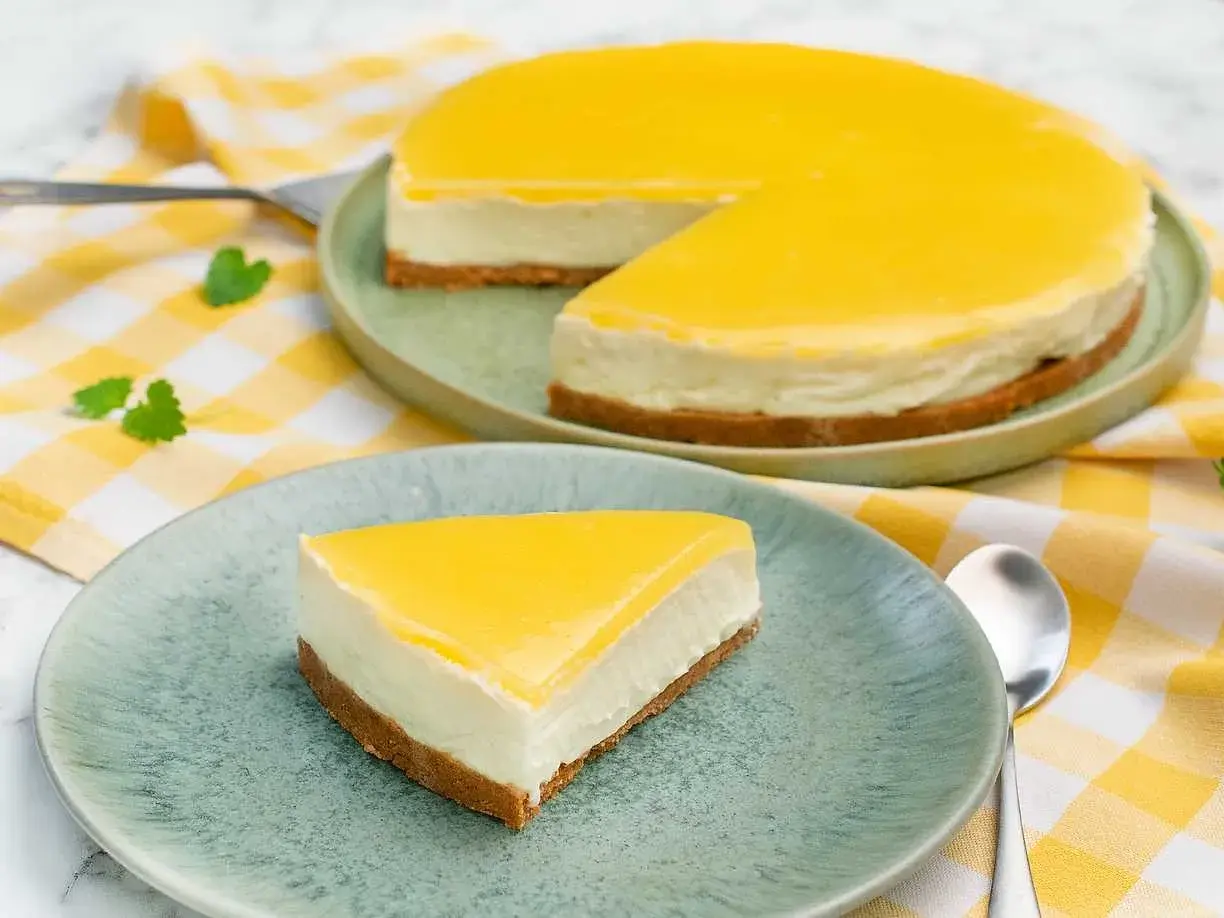 En krämig cheesecake med en syrlig lemon curd-topping, serverad på en ljusgrön tallrik med en gulrutig duk.