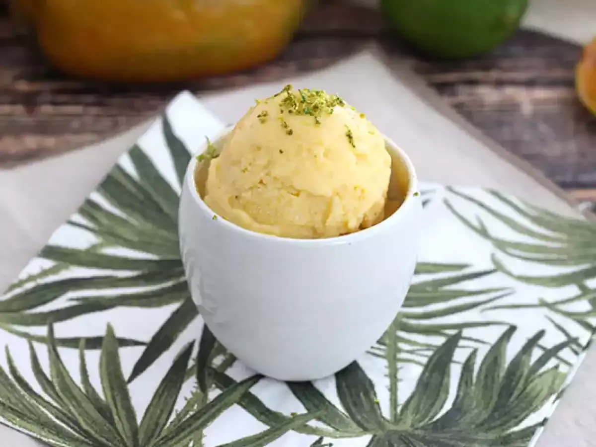 En skopa krämig mango glass i en vit skål, toppad med gröna strössel. Perfekt för en varm sommardag.