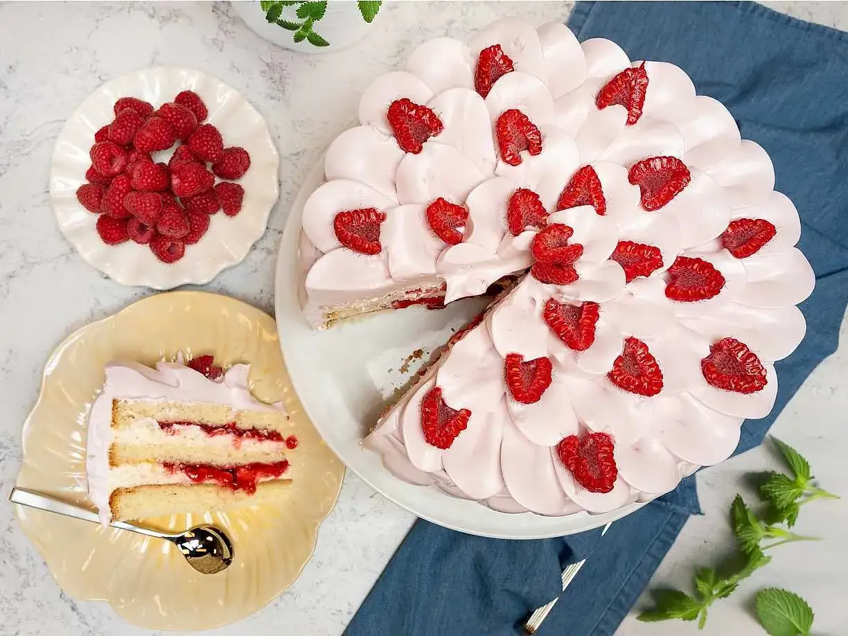 En himmelsk hallontårta med rosa frosting och färska hallon. En bit serverad på en gul tallrik med en sked.