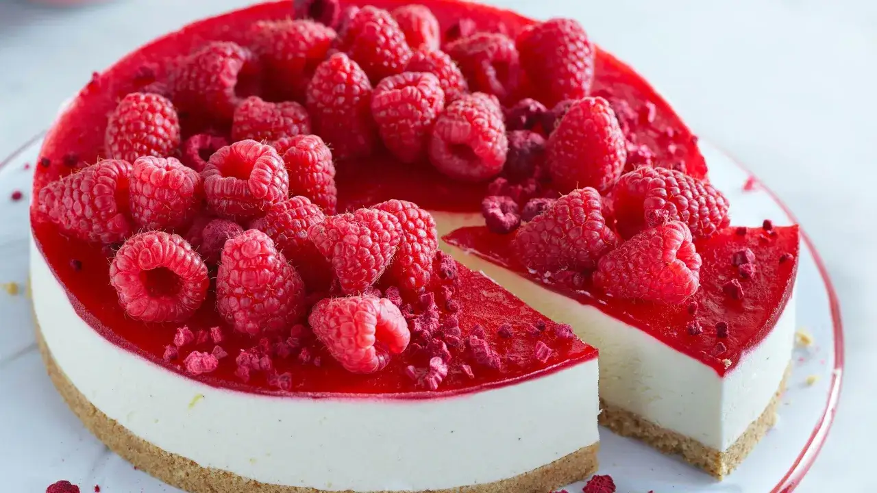 En kr&auml;mig new york cheesecake med hallontopping och f&auml;rska hallon. En bit &auml;r uppskuren.