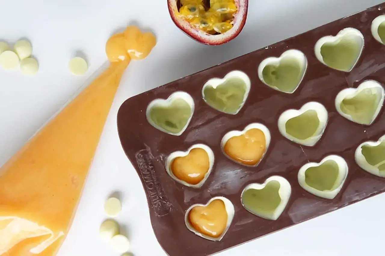 G&ouml;r egna fyllda praliner recept! En sprits med orange fyllning bredvid en hj&auml;rtformad pralinform med gr&ouml;na och orange fyllningar.