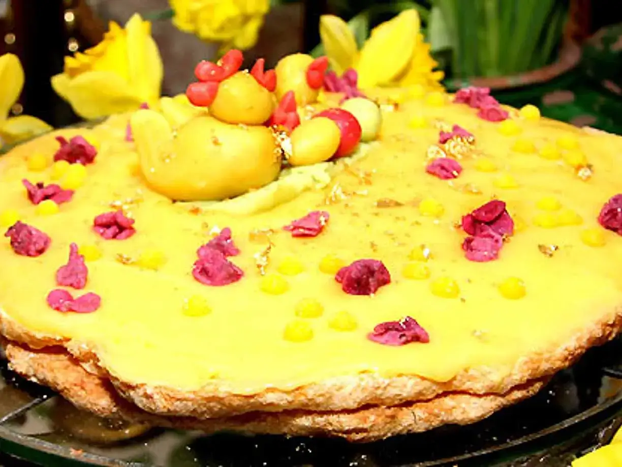 En gul t&aring;rta med en kycklingfigur p&aring; toppen, dekorerad med rosa blommor och gula prickar. En perfekt 