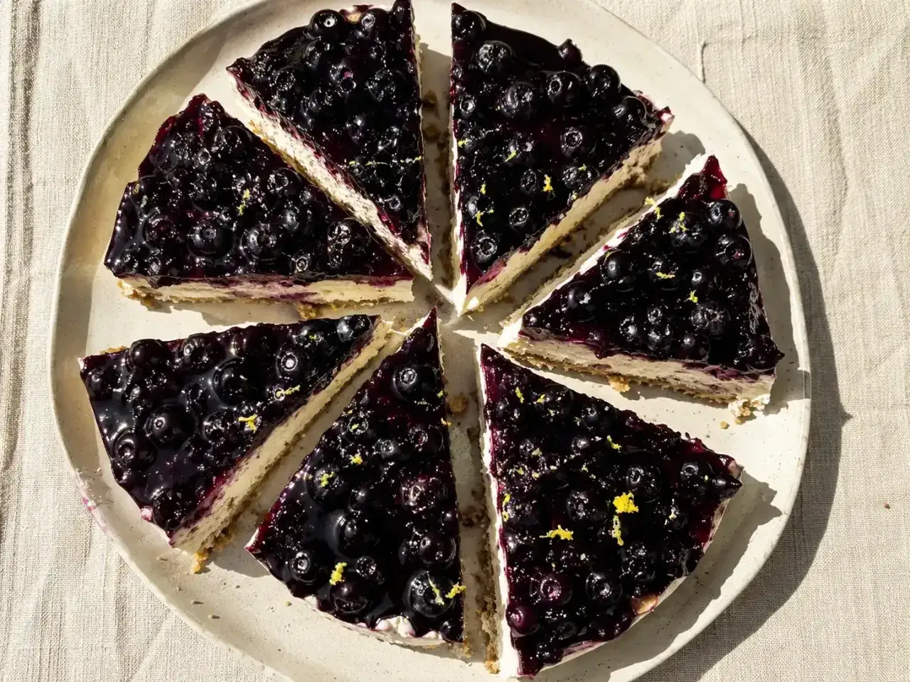 Bl&aring;b&auml;rscheesecake med digestivebotten utan ugn, toppad med glansig bl&aring;b&auml;rss&aring;s och citronskal.