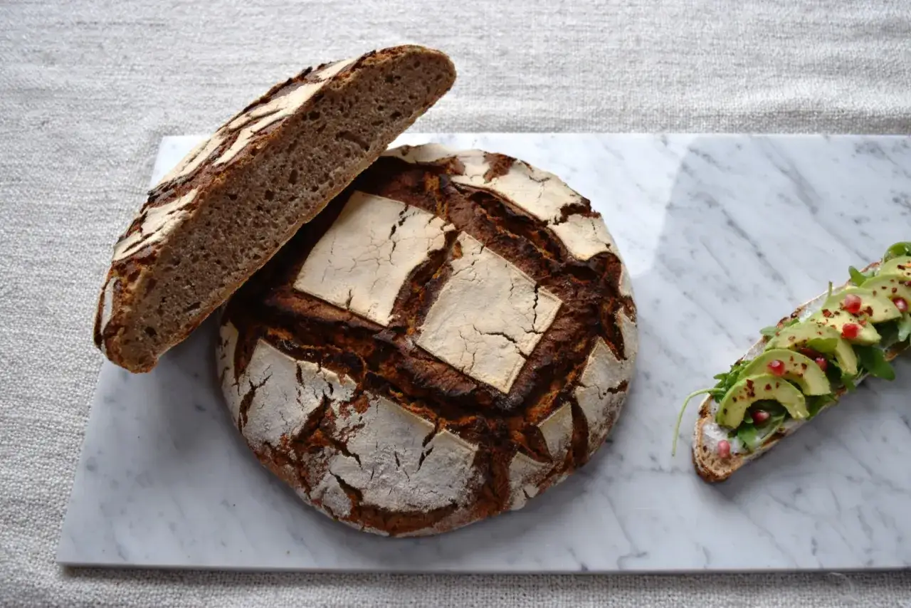Ett rustikt surdegsbr&ouml;d, bakat ist&auml;llet f&ouml;r vetemj&ouml;l, med en skiva avokadotoast.
