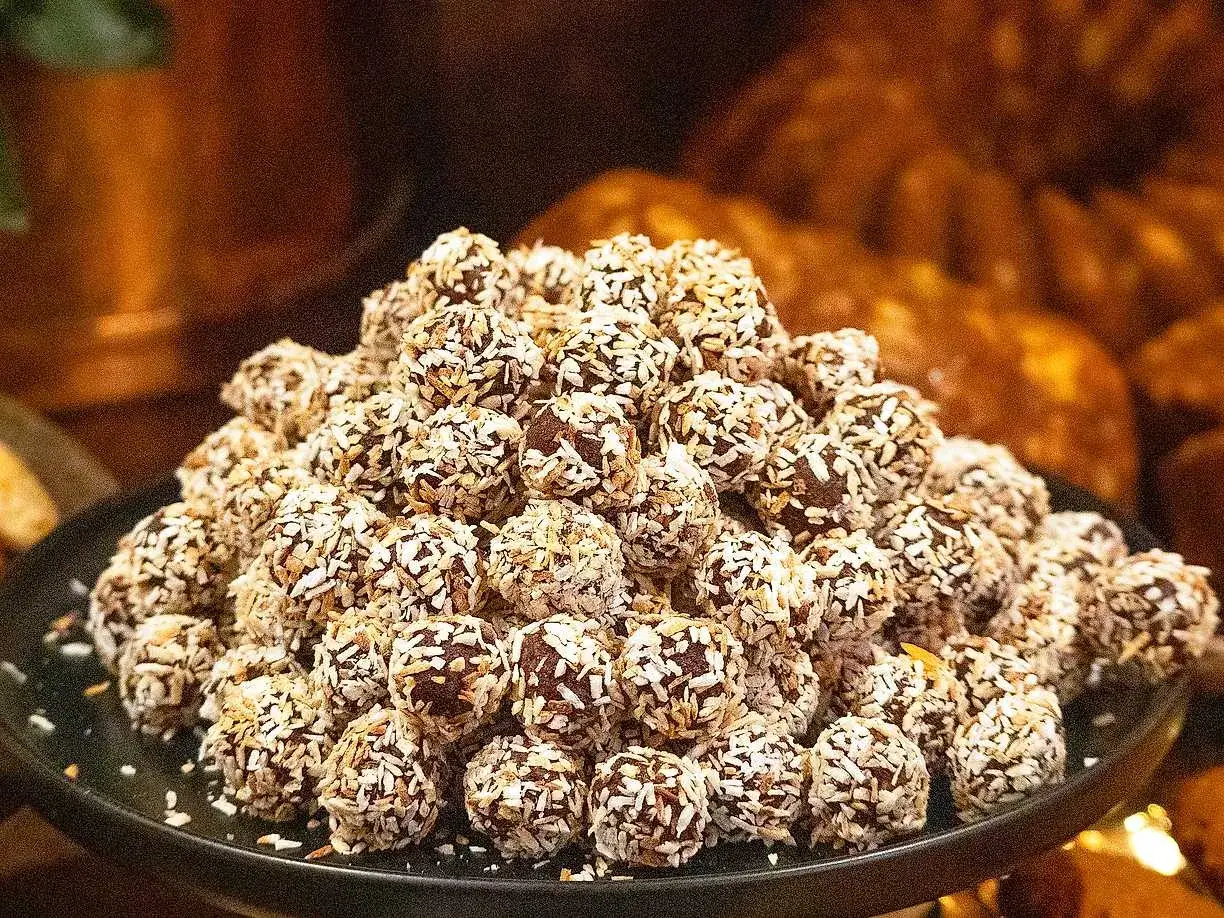 En h&ouml;g med lyxiga chokladbollar, rullade i kokosflingor, ligger upplagda p&aring; en m&ouml;rk tallrik.