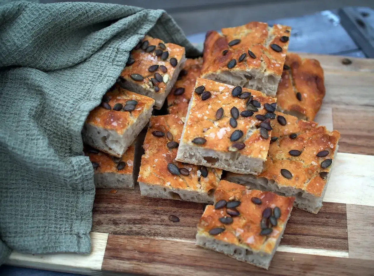 Focaccia med pumpak&auml;rnor och havssalt, bakad med dinkelmj&ouml;l ist&auml;llet f&ouml;r vetemj&ouml;l. Mjukt inlindad i en gr&ouml;n handduk.