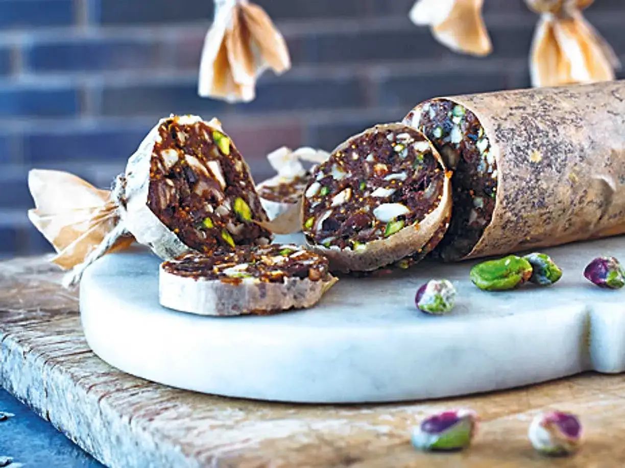 Chokladsalami med n&ouml;tter och torkad frukt, skuren i skivor och serverad p&aring; en marmorplatta.