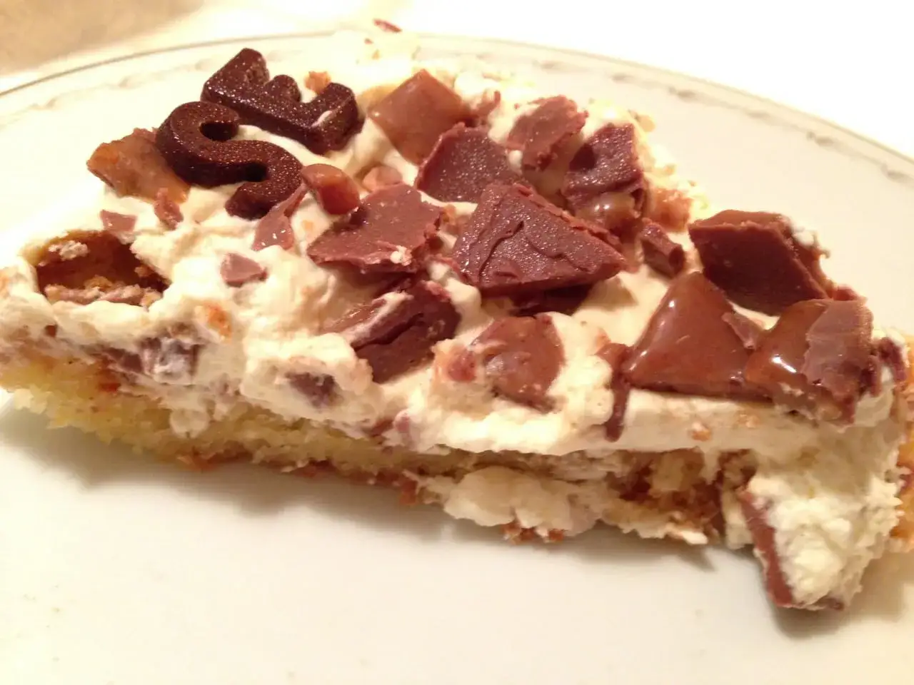 En bit kr&auml;mig daim t&aring;rta med chokladbitar och en chokladdekoration.