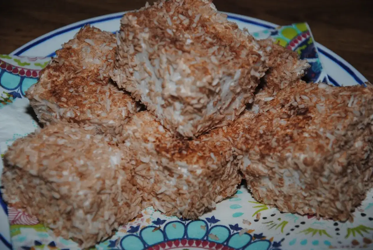 En h&ouml;g med fluffiga kokosbollar, t&auml;ckta av rostad kokos, ligger p&aring; en f&auml;rgglad servett.