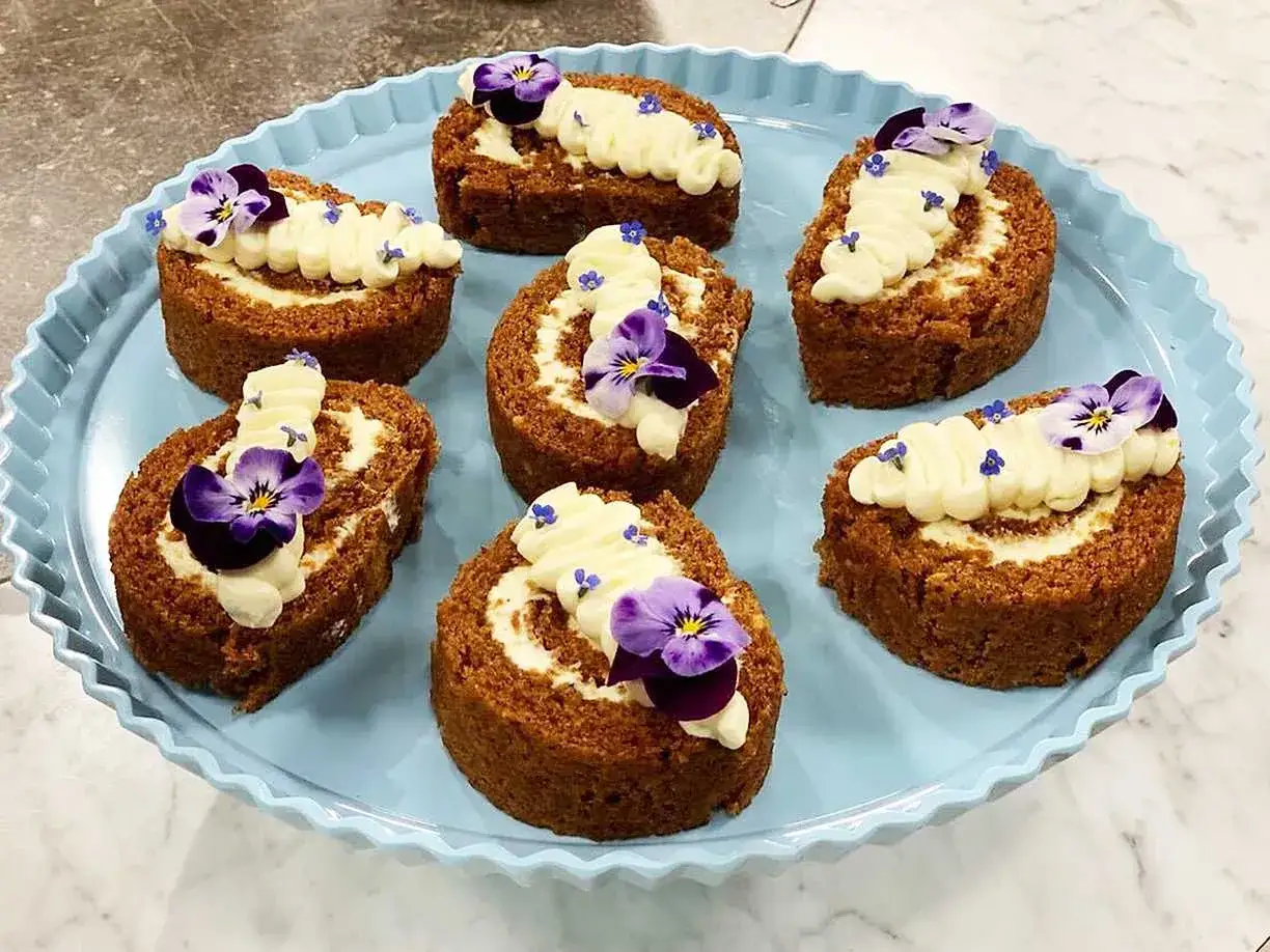 Sju sm&aring; morotskaka rullt&aring;rtor med kr&auml;mig frosting och violer p&aring; en ljusbl&aring; bricka. En h&auml;rlig dessert!