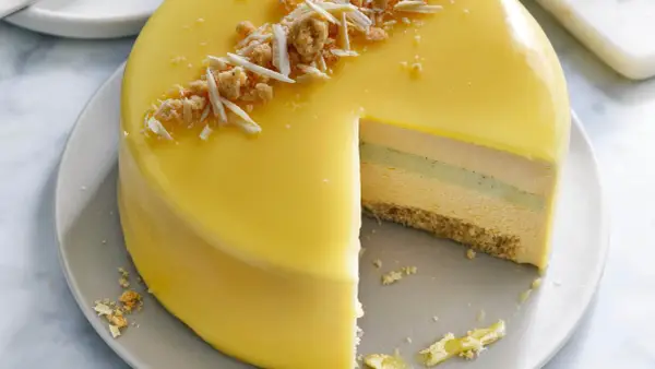 En vacker moussetårta med passionsfrukt, täckt av gul glasyr och toppad med smulor och vit choklad.